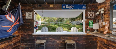 Eine rustikale Bar mit großem Fenster und Blick auf einen Garten, Holzwänden und einem Schild mit der Aufschrift 'Rugby Rd.'