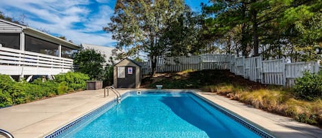 A swimming pool with a small adjacent structure, surrounded by a fence and trees.