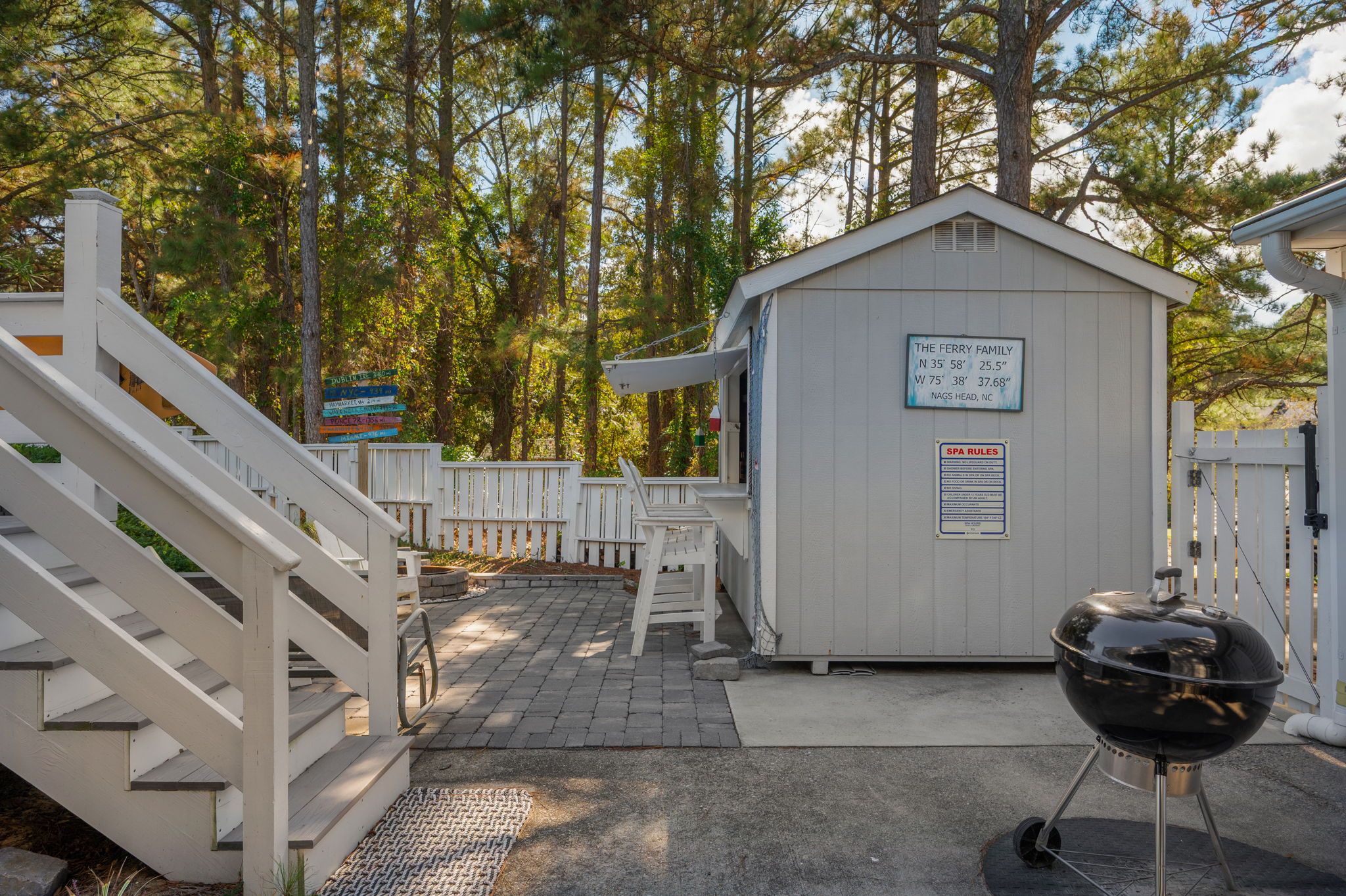 A covered outdoor area with a barbecue grill, a small shed, and a white fence.