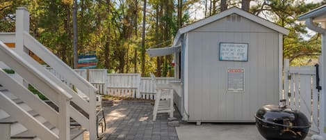 A covered outdoor area with a barbecue grill, a small shed, and a white fence.