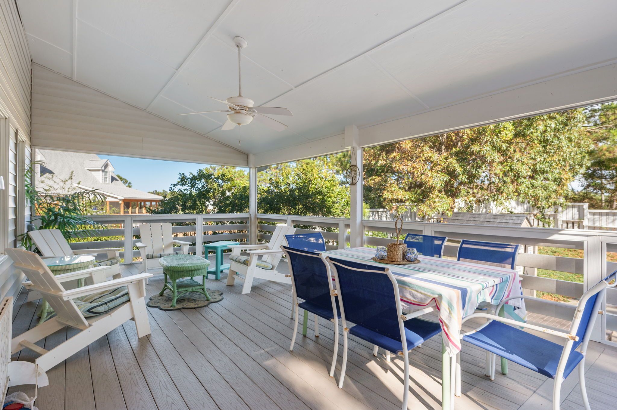 A covered outdoor deck with white railings, blue and white chairs, and a table with a striped tablecloth.