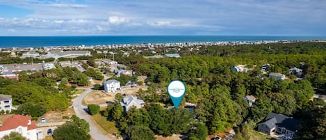 An aerial view of a coastal residential area with houses, a road, and a body of water in the background.