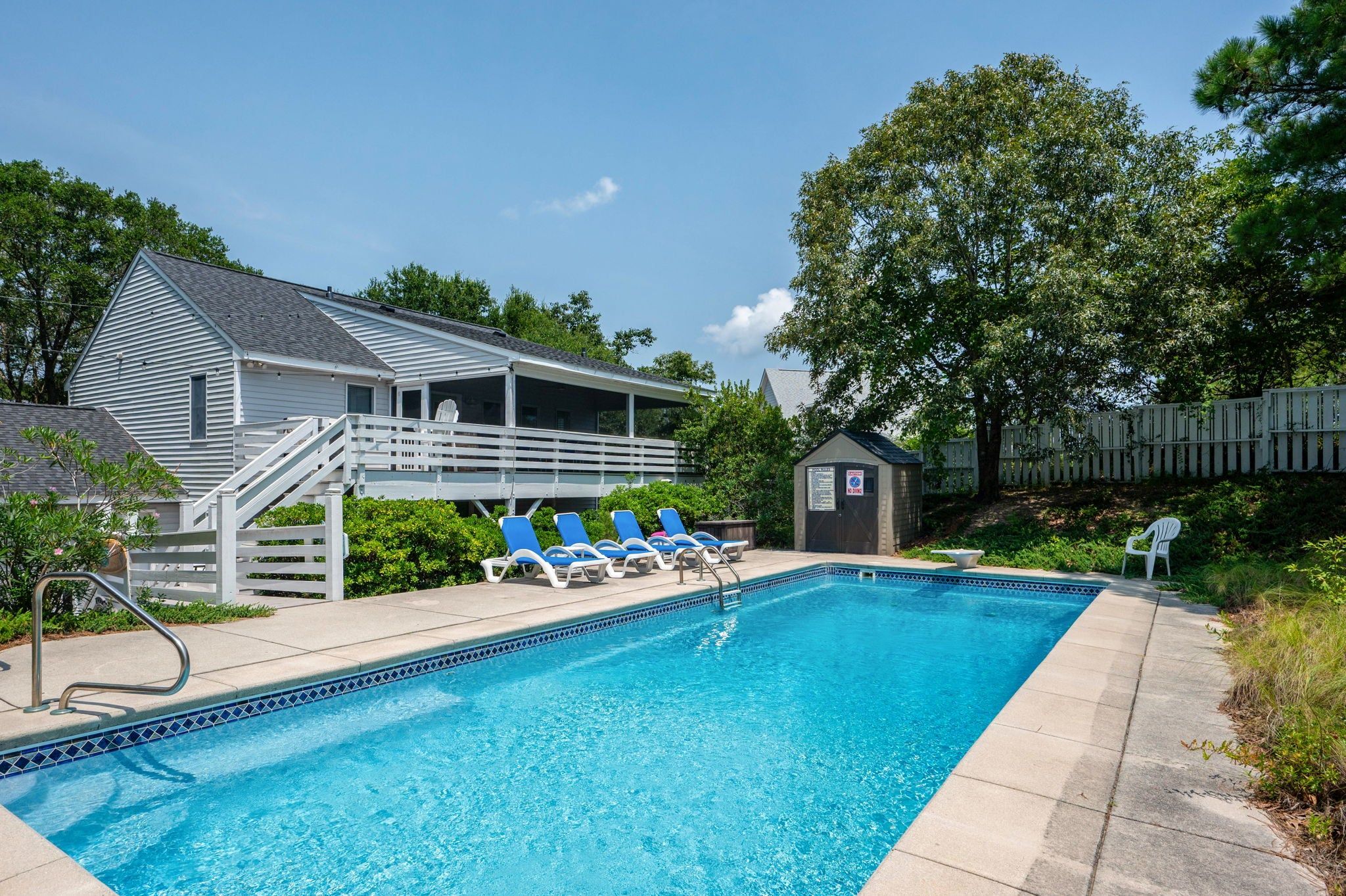 A swimming pool with lounge chairs, a covered deck, and a small shed.