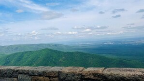 Eine Steinmauer mit Blick auf eine gebirgige Landschaft unter blauem Himmel.