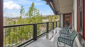 A balcony with a metal railing, a row of green metal chairs, and a view of trees and mountains.