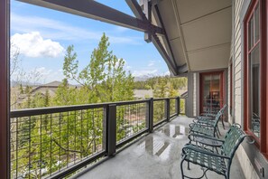 Un balcon avec une balustrade en métal, une rangée de chaises en métal vertes et une vue sur les arbres et les montagnes.