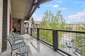 A balcony with outdoor furniture, a view of a parking area, and a building with a traditional architectural style.