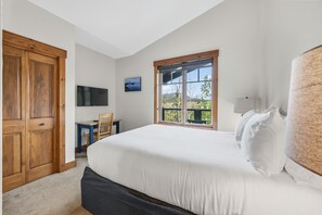 A bedroom with a large bed, wooden wardrobe, a desk, and a window with a view.