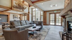 A spacious living area with a fireplace, large windows, and a chandelier.
