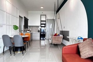 Une cuisine moderne avec des meubles blancs, un coin repas avec des chaises grises et orange, et un canapé rouge agrémenté d’un coussin.