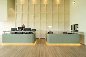 A reception area with two counters, a large wall with a grid pattern, and a wooden floor. - Amber Cove Luxury Design By Luxpro Management (Melaka Tengah)