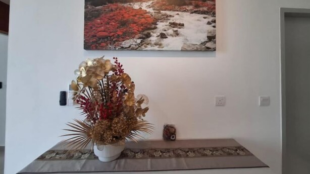 Una habitación con un cuadro de un paisaje fluvial, una mesa con un jarrón de flores secas y un pequeño objeto decorativo sobre la mesa.