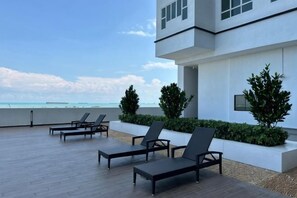 Un edificio moderno con un patio en la azotea, sillones de descanso y vistas al océano.