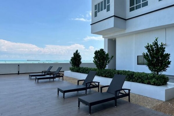 A modern building with a rooftop patio, lounge chairs, and a view of the ocean. - Amber Cove Luxury Design By Luxpro Management (Melaka Tengah)
