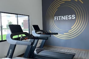 Un área de fitness con cintas de correr y una pared con la palabra 'FITNESS' en letras grandes.