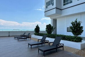 A modern building with a rooftop patio featuring lounge chairs and a view of the beach. - Amber Cove Luxury Design By Luxpro Management (Melaka Tengah)