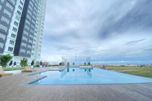 Une piscine sur le toit, avec une terrasse en bois, entourée d’un immeuble de grande hauteur et sous un ciel dégagé.