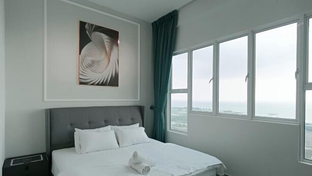 A modern hotel room with a large bed, a nightstand, a framed artwork, and a view through large windows. - Amber Cove Luxury Design By Luxpro Management (Melaka Tengah)