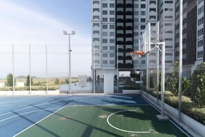 An outdoor basketball court with a net, surrounded by a fence, and adjacent to a high-rise building. - Amber Cove Luxury Design By Luxpro Management (Melaka Tengah)