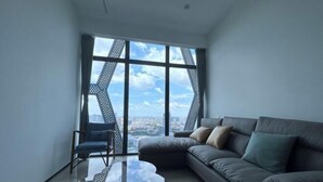 A modern living room with a large window, a sofa, a chair, and a glass coffee table. - Golden Bridge Business Hotel (Phnom Penh)