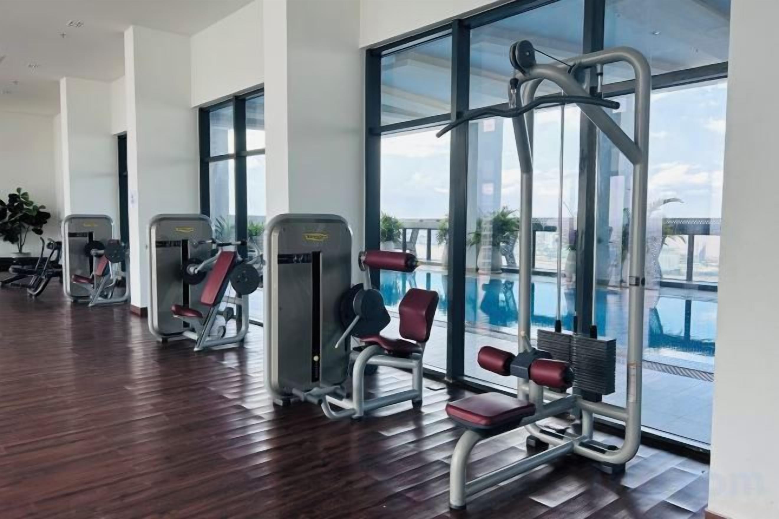 Ginásio com equipamentos de exercício e amplas janelas com vista para uma piscina.