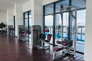 A gym with exercise equipment and large windows overlooking a swimming pool. - Golden Bridge Business Hotel (Phnom Penh)