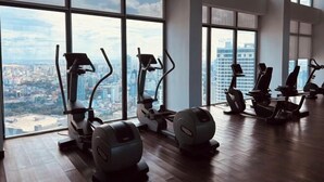 A gym with cardio machines and large windows overlooking a cityscape. - Golden Bridge Business Hotel (Phnom Penh)