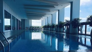 A modern indoor swimming pool with clear glass walls, potted plants, and a view of the cityscape. - Golden Bridge Business Hotel (Phnom Penh)