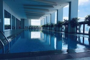 Una piscina interior con paredes de cristal transparente, plantas en macetas y vistas al cielo.
