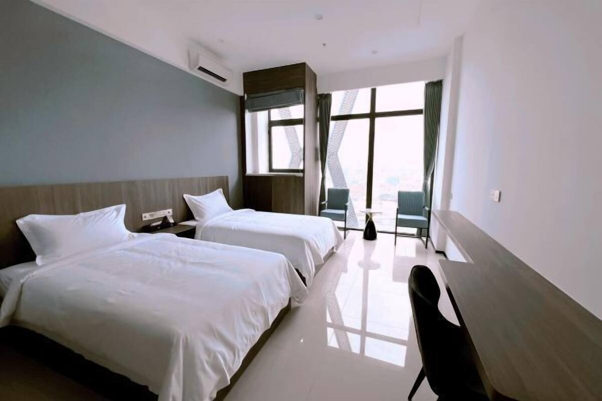 A hotel room with two beds, a desk, and a large window with curtains.