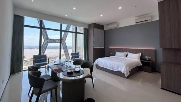 A modern hotel room with a large bed, a dining table with chairs, and a view of the cityscape. - Golden Bridge Business Hotel (Phnom Penh)