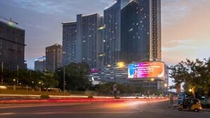 A cityscape with modern high-rise buildings, a prominent billboard, and a busy street with light trails from moving vehicles. - Golden Bridge Business Hotel (Phnom Penh)