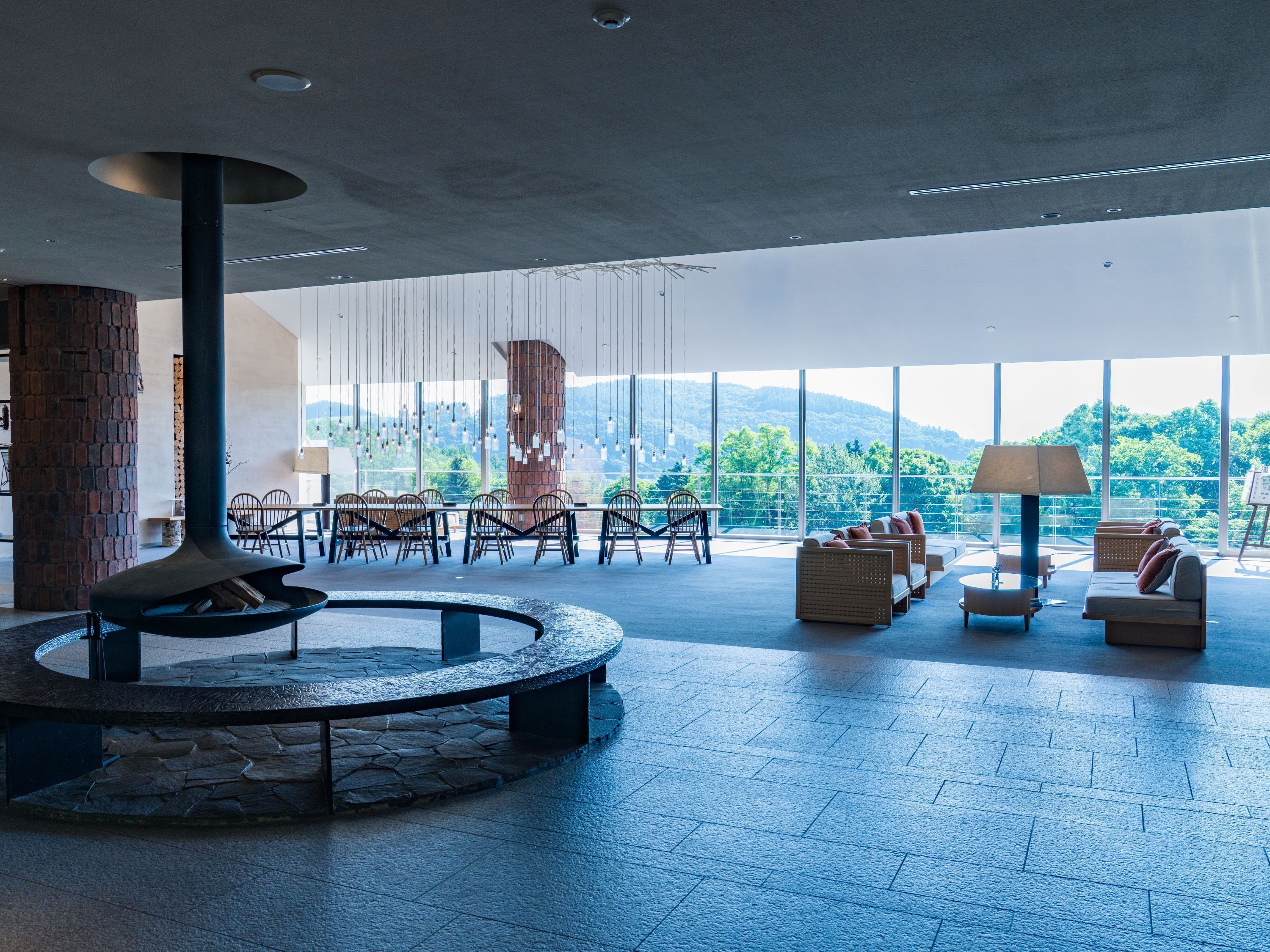 Amplio espacio interior con un hogar de piedra, disposiciones para sentarse y grandes ventanales que ofrecen vistas al exterior.