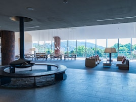 A spacious indoor area with a stone fire pit, seating arrangements, and large windows offering a view of the outdoors.