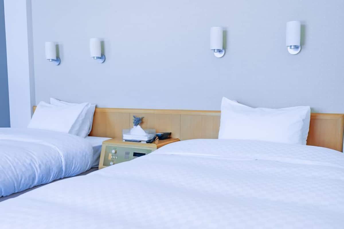A hotel room with two beds, a wooden headboard, bedside tables, and wall-mounted light fixtures.