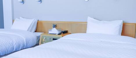 A hotel room with two beds, a wooden headboard, bedside tables, and wall-mounted light fixtures.