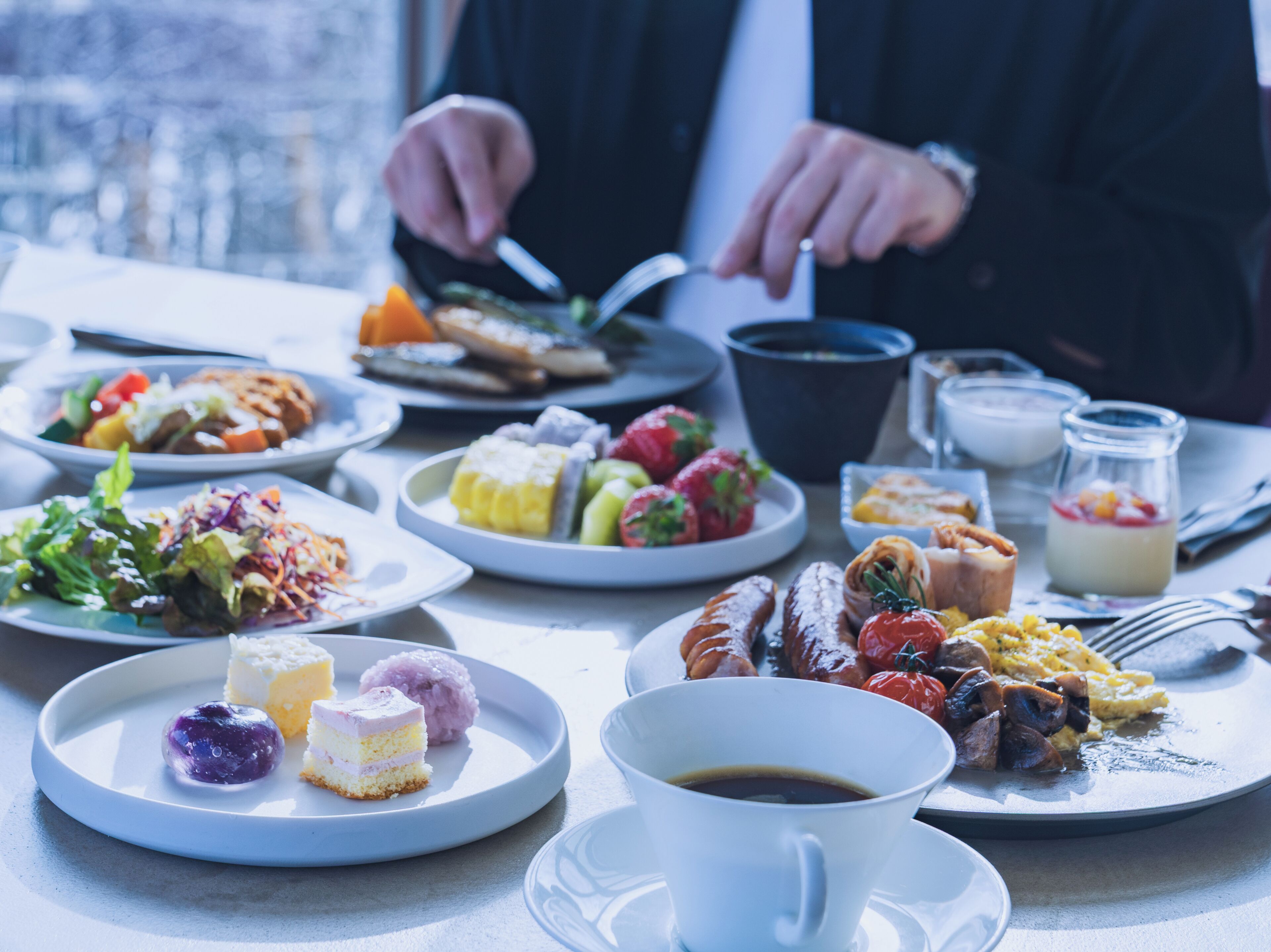 A dining table with various dishes, a cup of coffee, and a person cutting food.