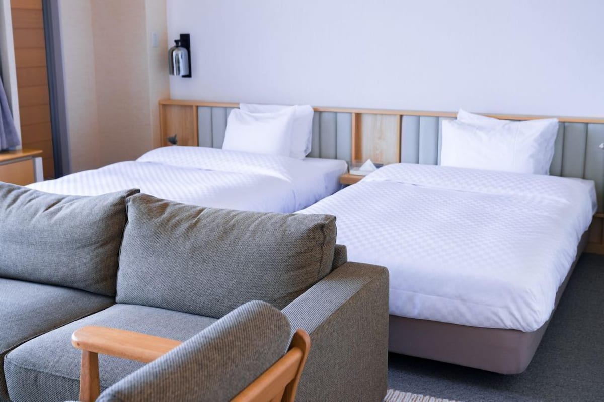 A hotel room with two beds, a sofa, and a bedside table.