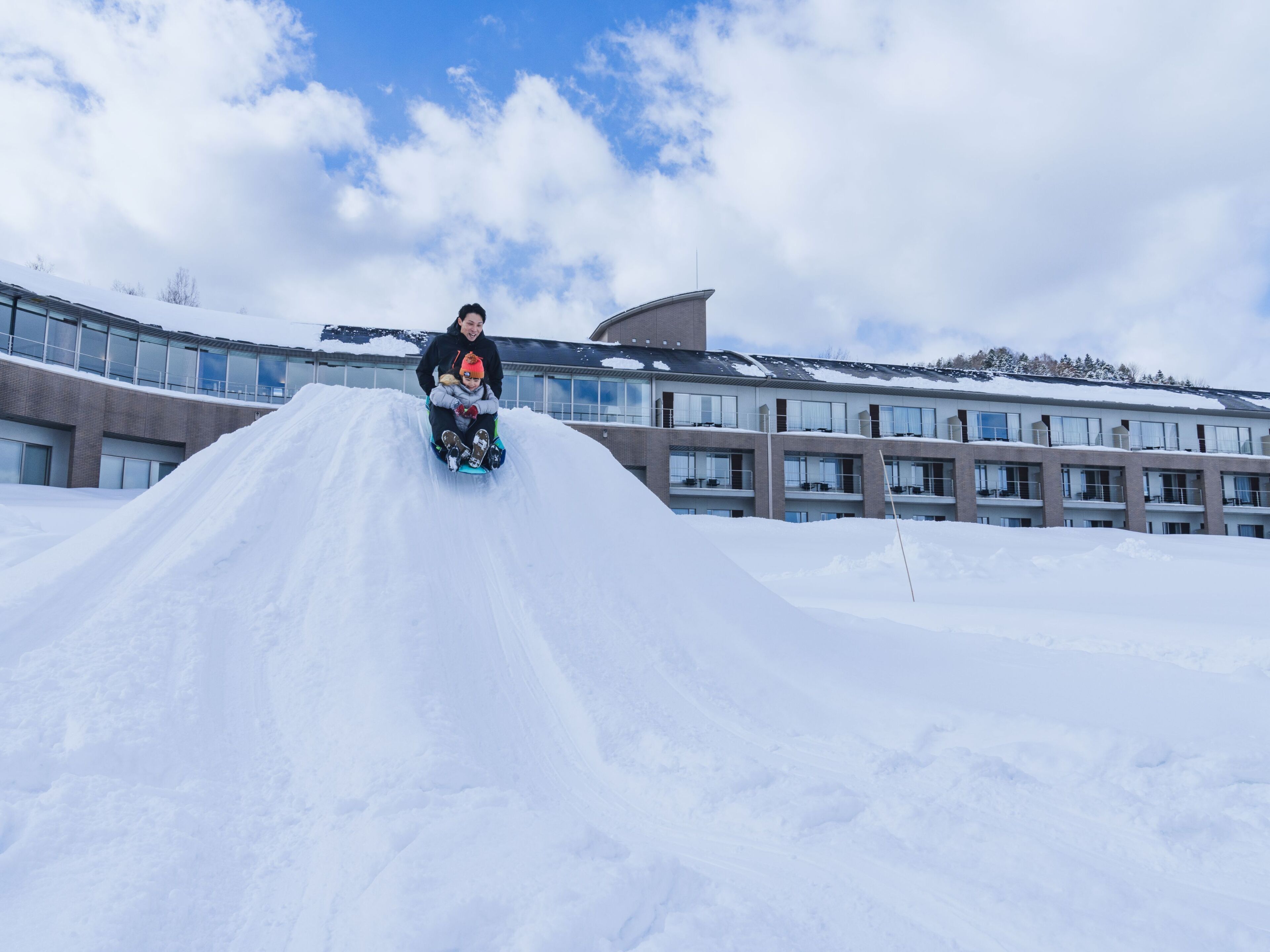 Una persona deslizándose por una rampa de nieve con un edificio al fondo.