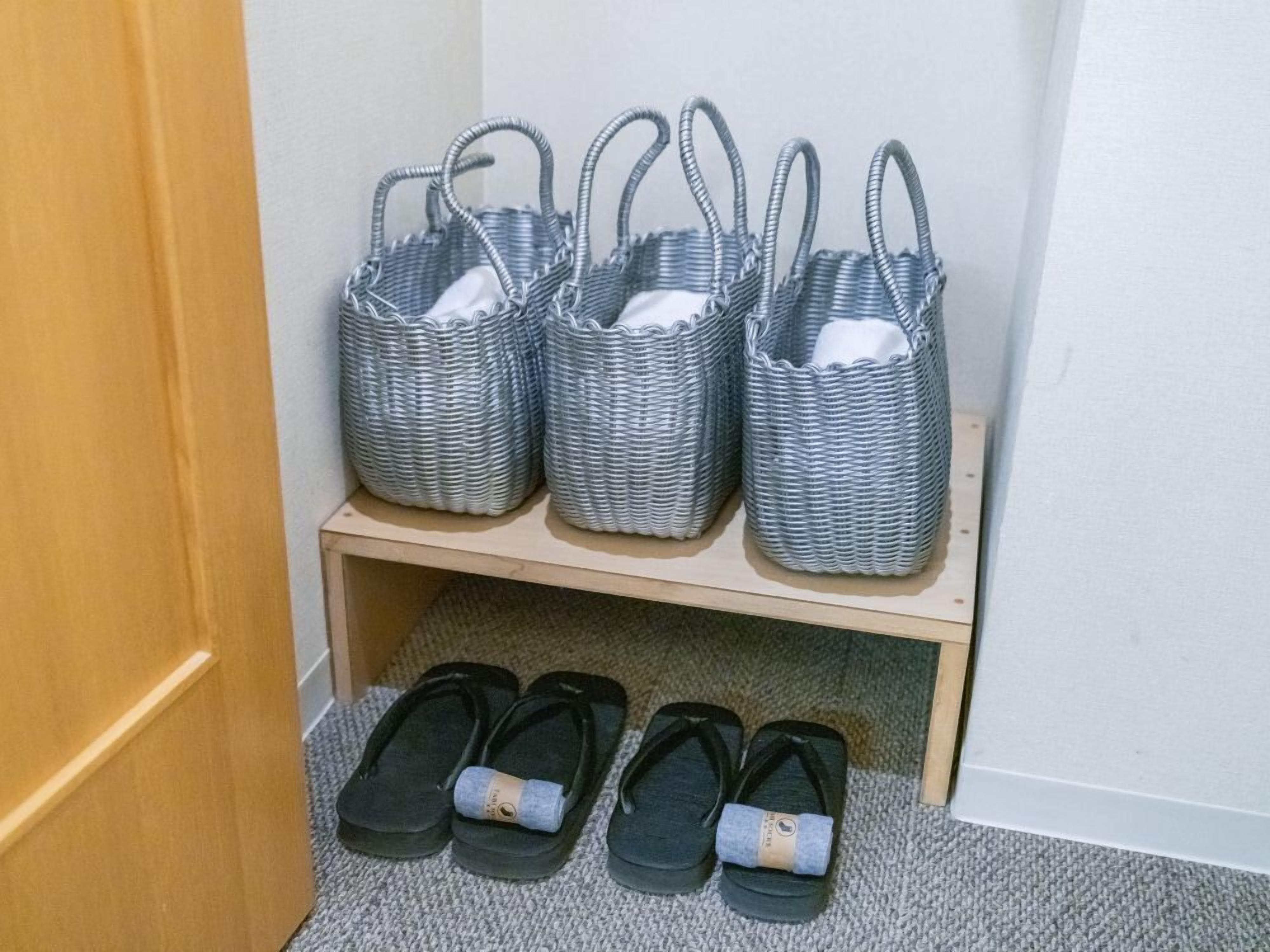 Une étagère de rangement avec quatre paniers en osier et trois paires de chaussons noirs.