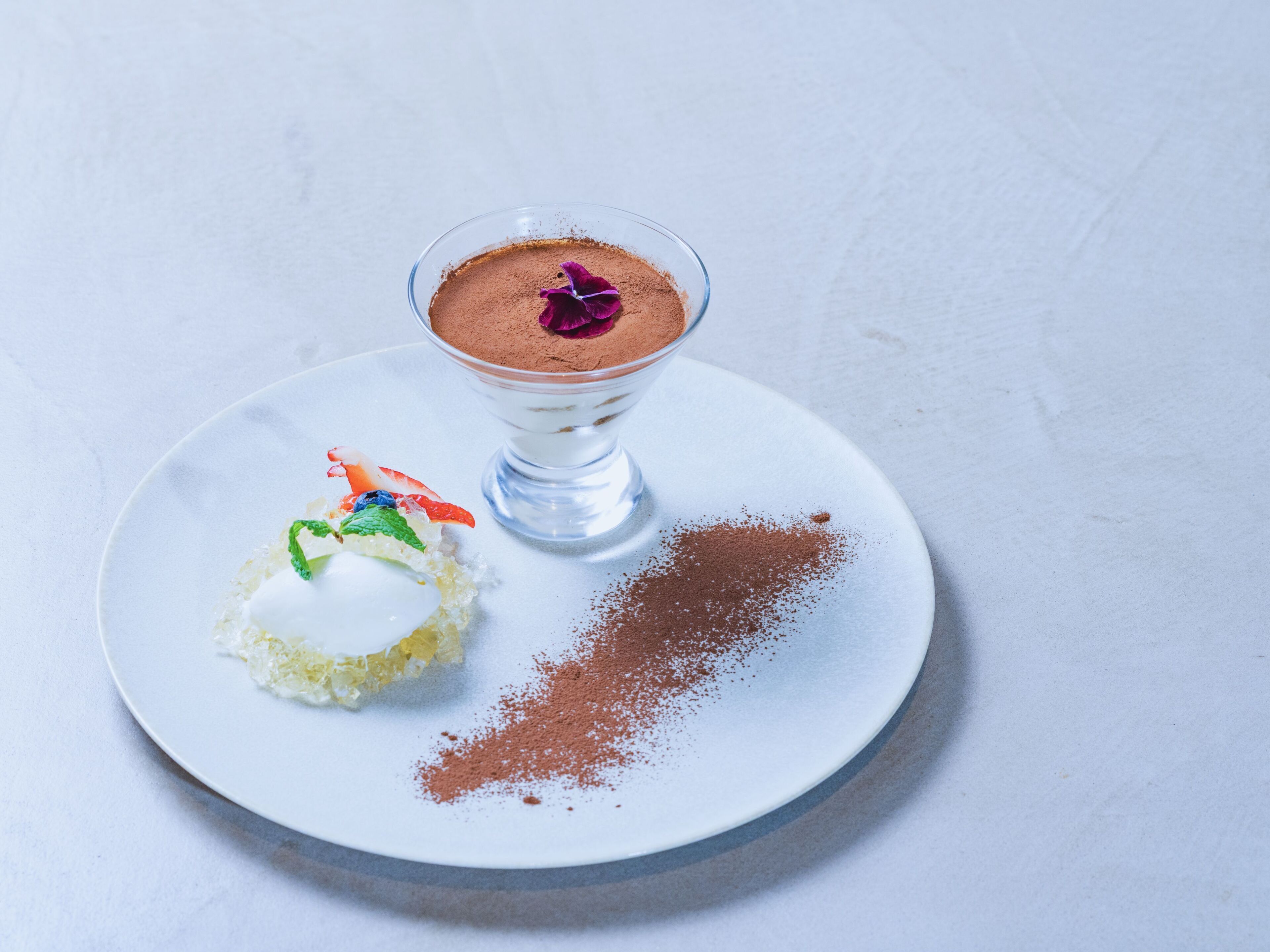 Un postre sobre un plato blanco con un cuenco de vidrio transparente.