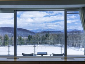 A room with a large window offering a view of a snowy landscape with trees and mountains. - FURANO HOTEL (Furano)