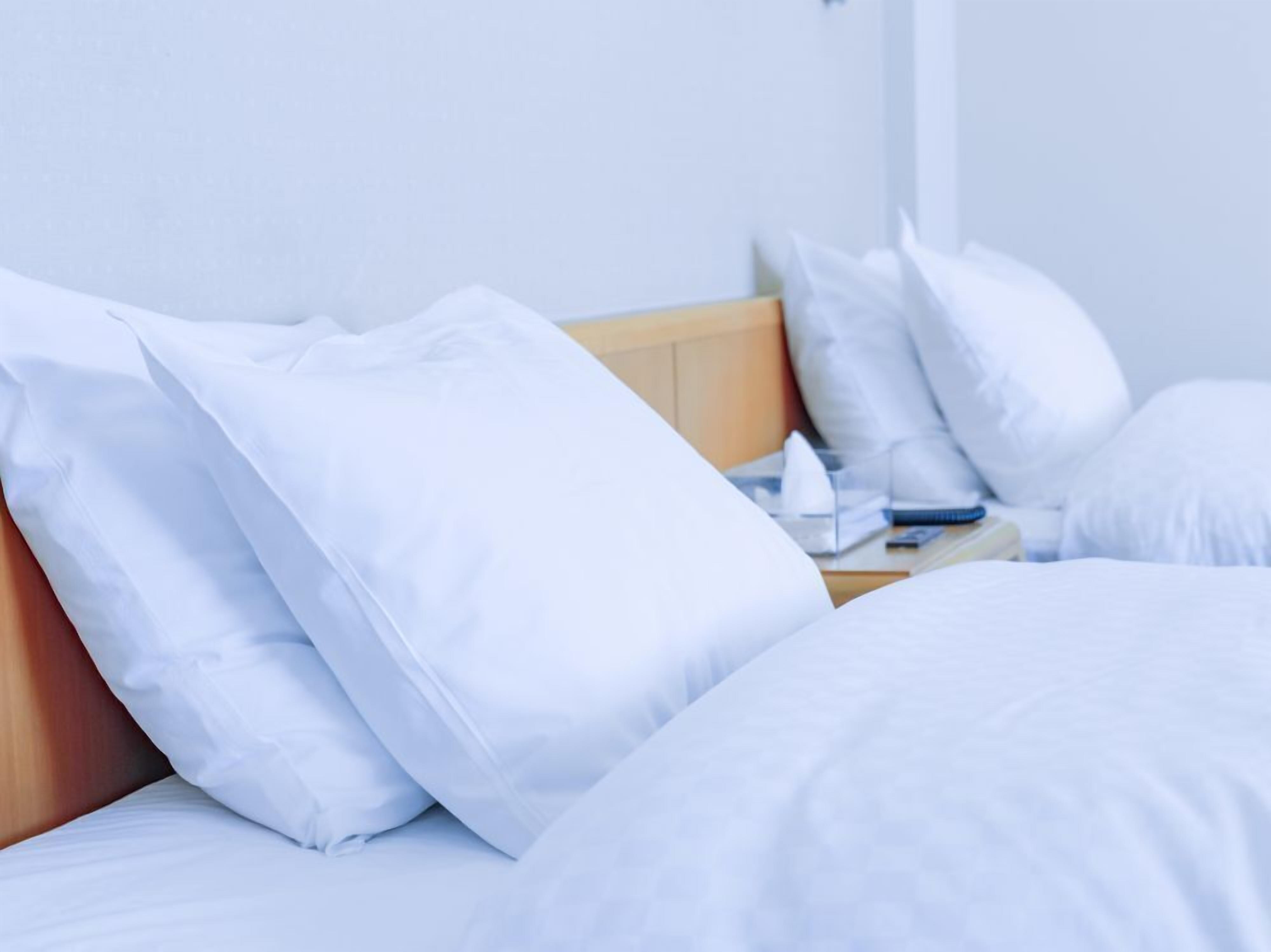 Una cama con ropa blanca y almohadas, un cabecero de madera y una mesita de noche con una lámpara y un libro.