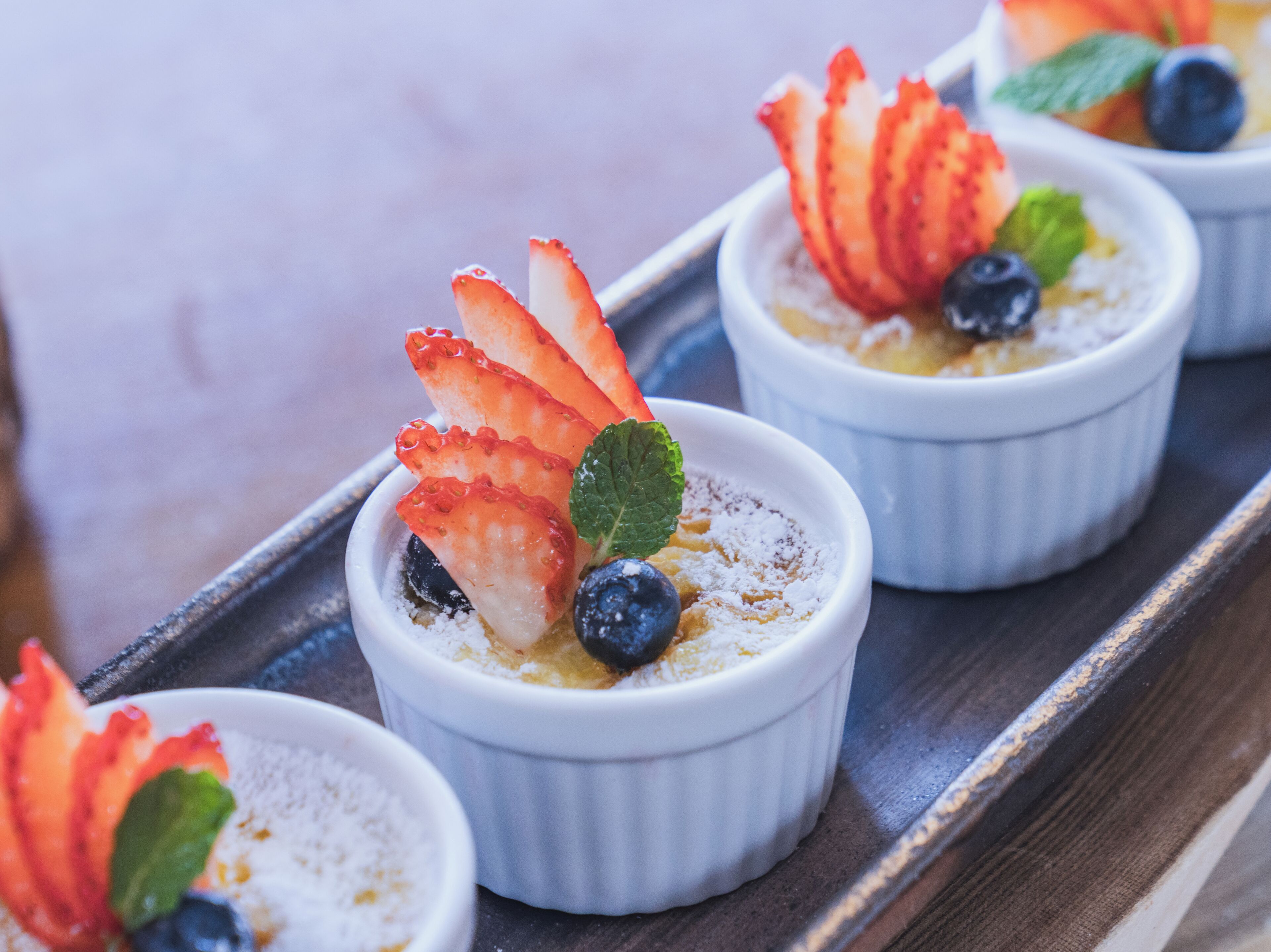 Three ramekins with dessert garnished with strawberries and blueberries.