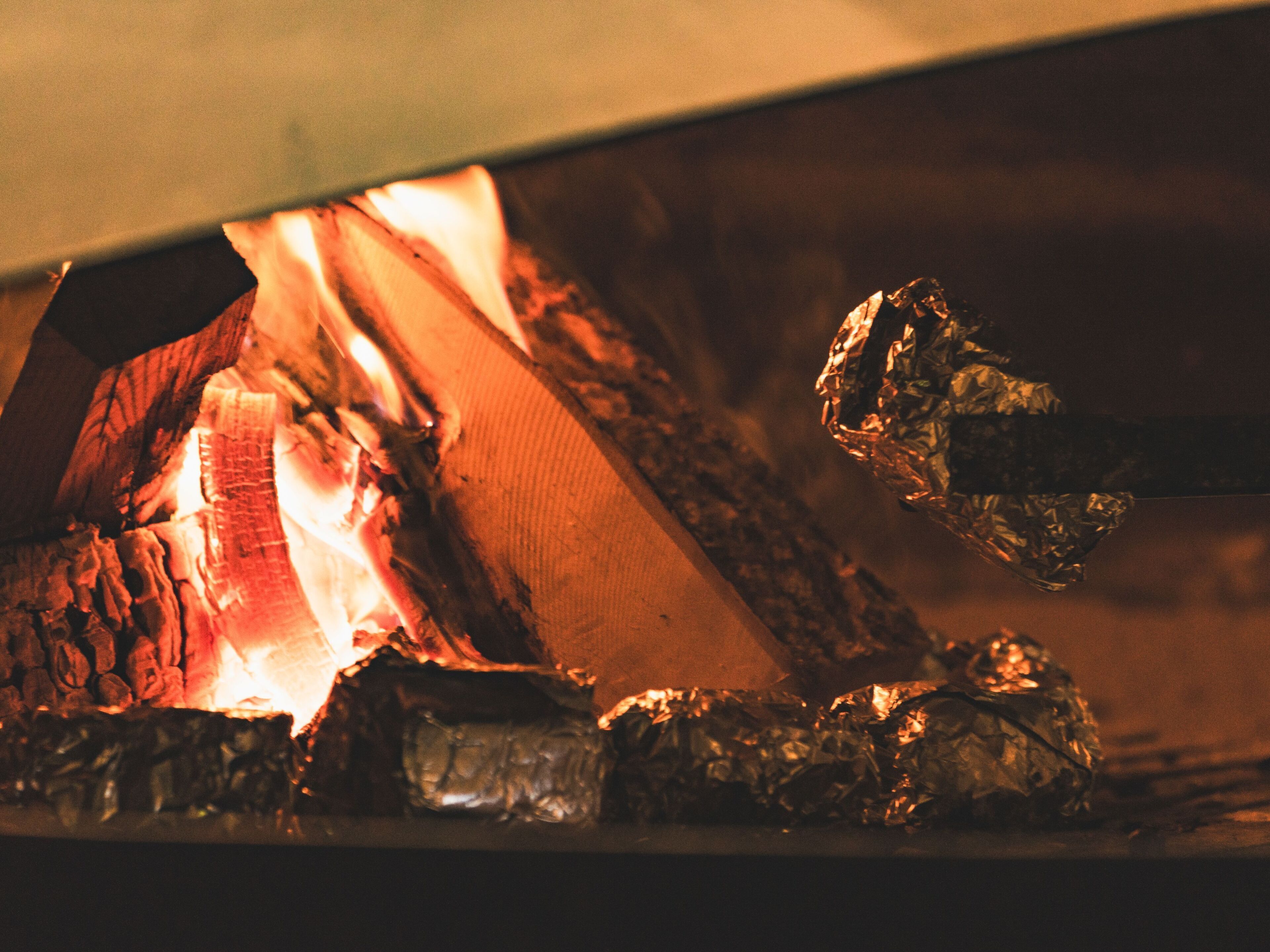 A close-up of a fire burning in a fireplace with logs and a piece of foil.