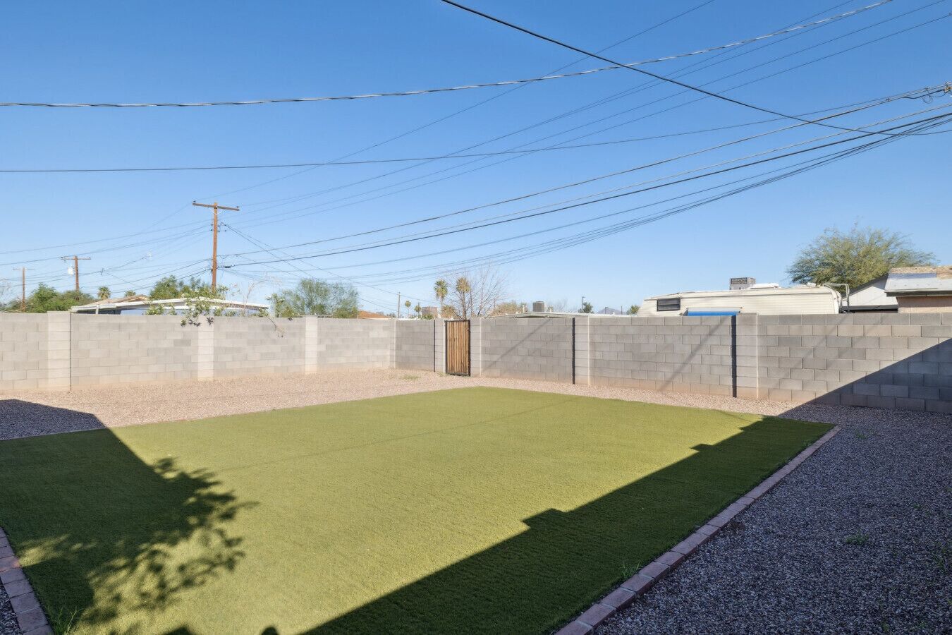 A fenced backyard with artificial grass, a gravel path, and a wooden gate.