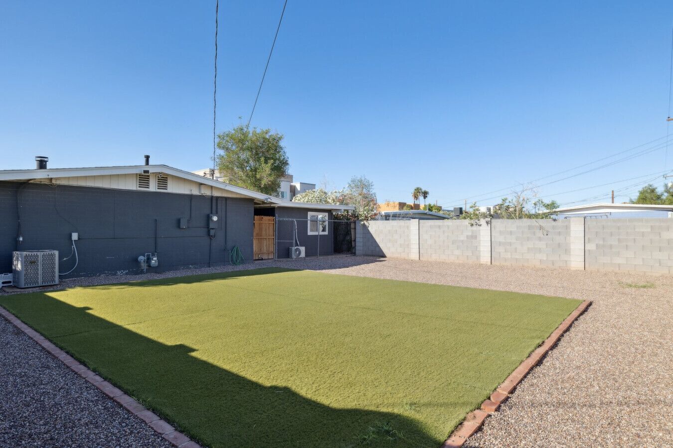 A backyard with artificial grass, a grey building, and a concrete wall.