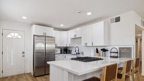 Une cuisine moderne avec des meubles blancs, un réfrigérateur en acier inoxydable, une cuisinière à gaz et des chaises en bois.