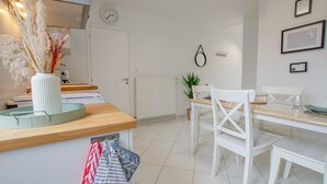 A modern kitchen with white cabinetry, a wooden countertop, and a dining area with white chairs.