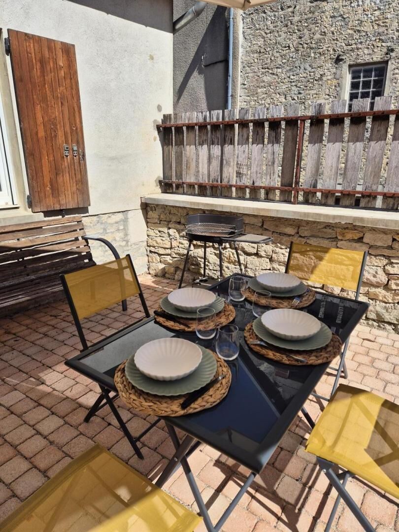 Un espace extérieur aménagé pour les repas, avec un mur en pierre en arrière-plan, un barbecue et une clôture en bois.